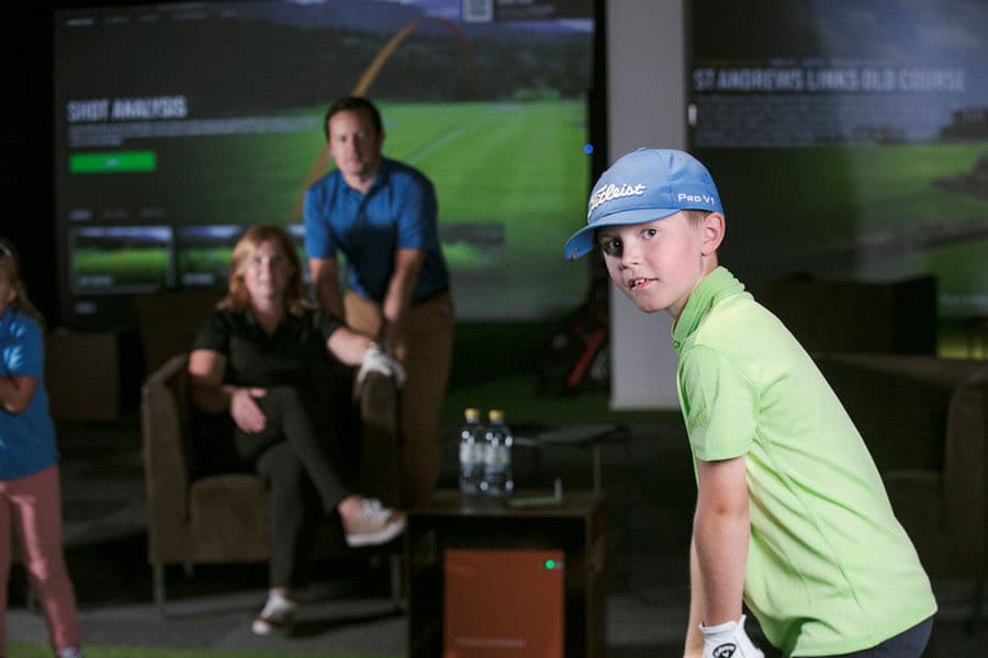 A young golfer and his family in a simulator bay at Caddi Club