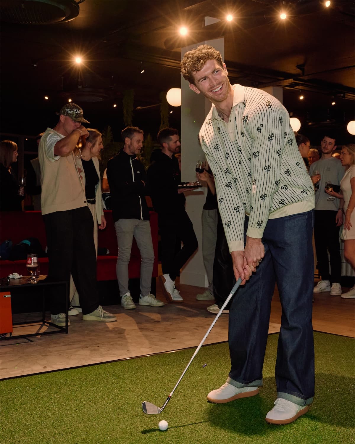 A golfer putting in a simulator bay at Caddi Club Fulham, his friends watching behind him