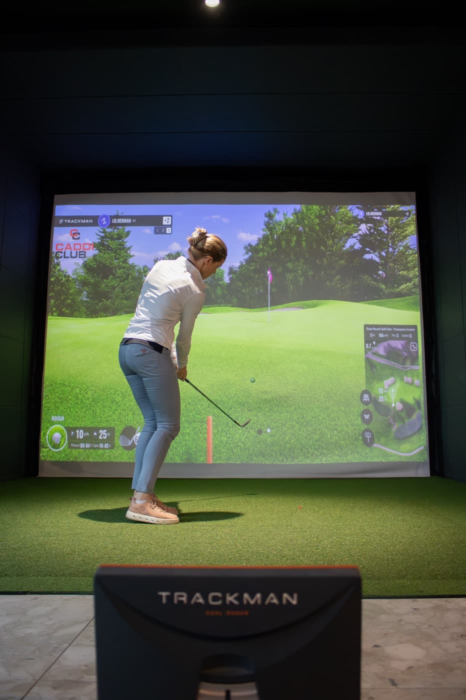 A member mid-swing in a bay, the TrackMan unit in front of her