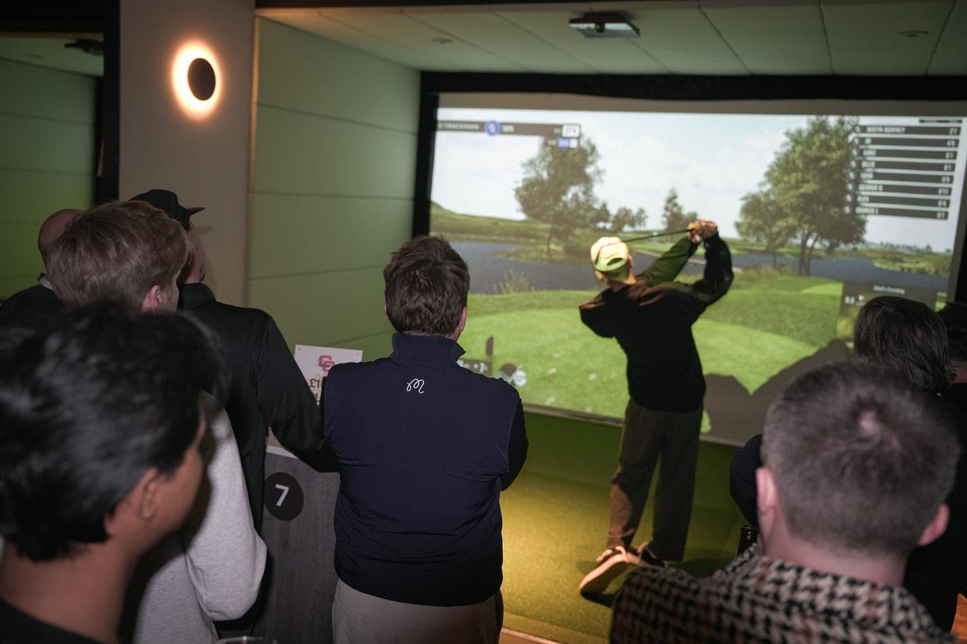 Members watching a drive on the simulator screen at Caddi Club