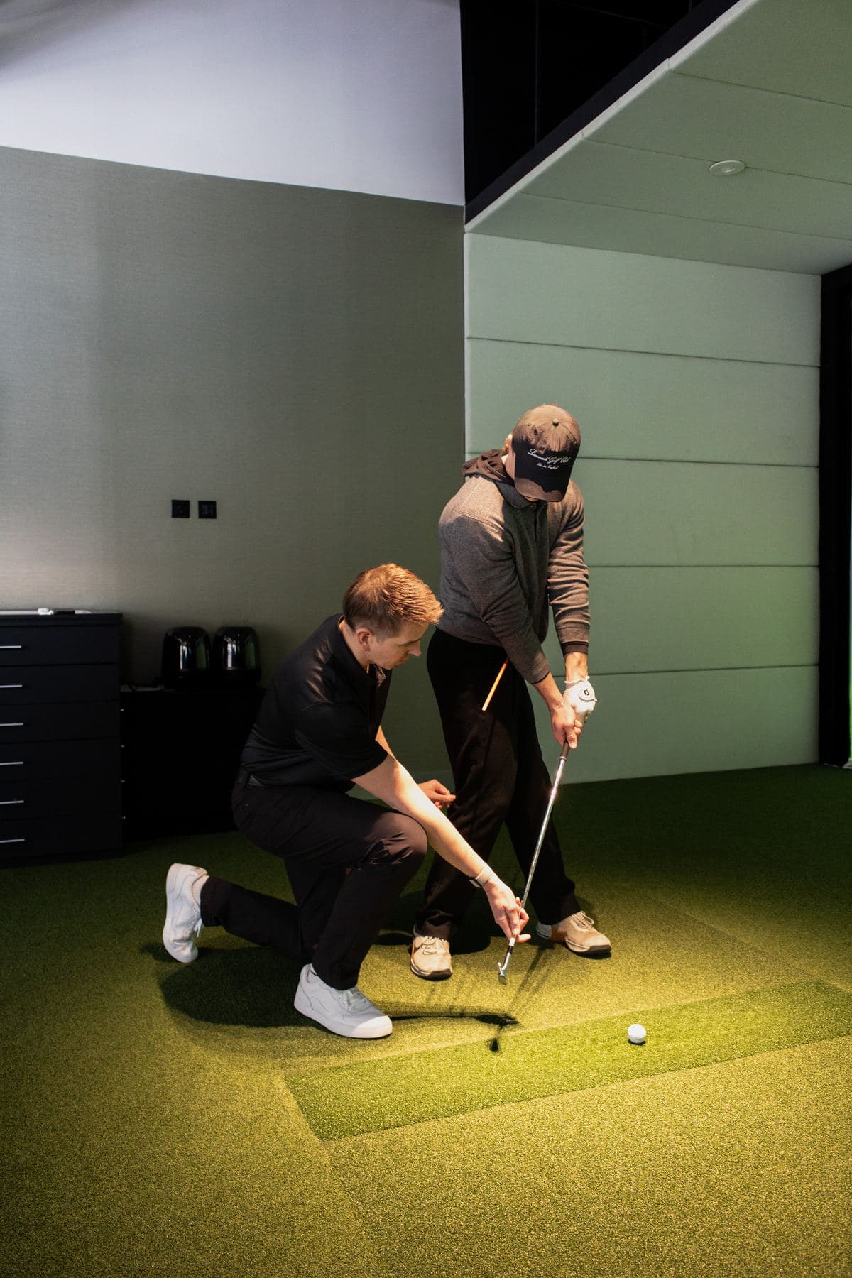 A PGA coach adjusting a beginner's stance in a bay